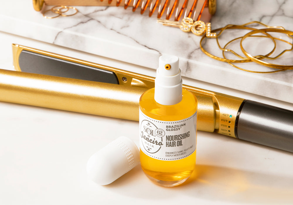 bottle of BRAZILIAN GLOSSY™ NOURISHING HAIR OIL in front of a hair straightening tool