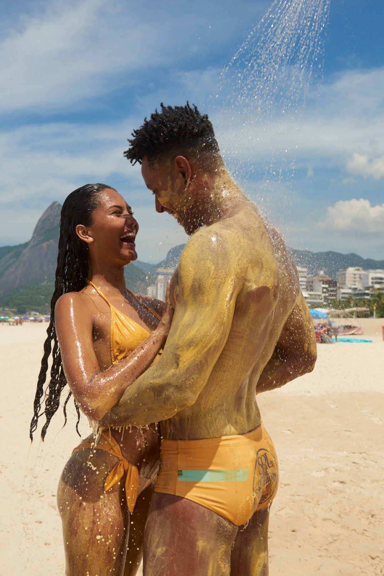 couple on the beach smiling and holding each other under a shower of water