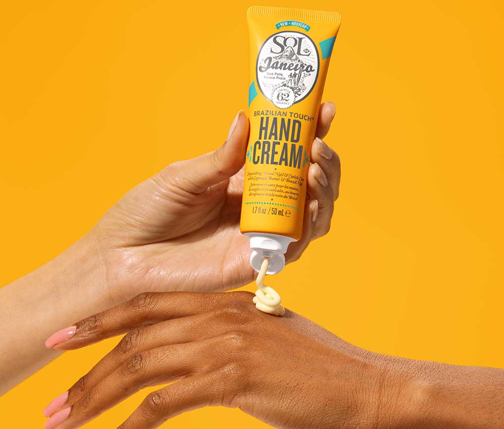 Brazilian Touch hand cream being applied to the back of a hand. On a yellow background