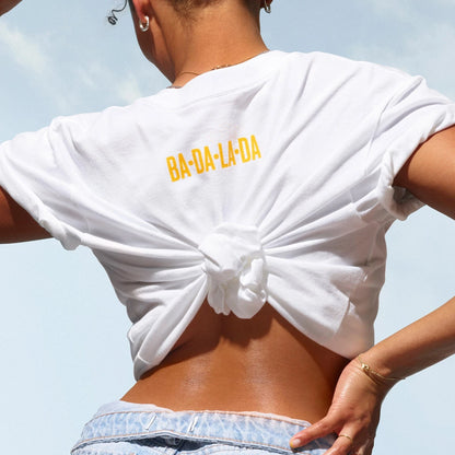 sol de janeiro badalada t-shirt, on the back of t-shirt it reads &quot;ba-da-la-da&quot; in sol de janeiro yellow. T shirt is white