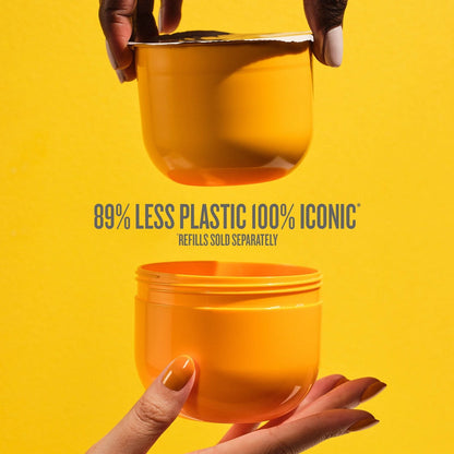 This image is a yellow background with two hands holding one end of the Sol de Janeiro Brazilian Bum Bum Cream refill pod and the refill insert. The text on the image reads as follows &quot;89% less plastic 100% iconic refills sold separately.&quot; in grey text