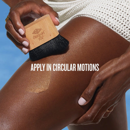 text on the image reads apply in circular motions. This image shows model using the brush to put on her sol de janeiro glowmotions body oil on her legs